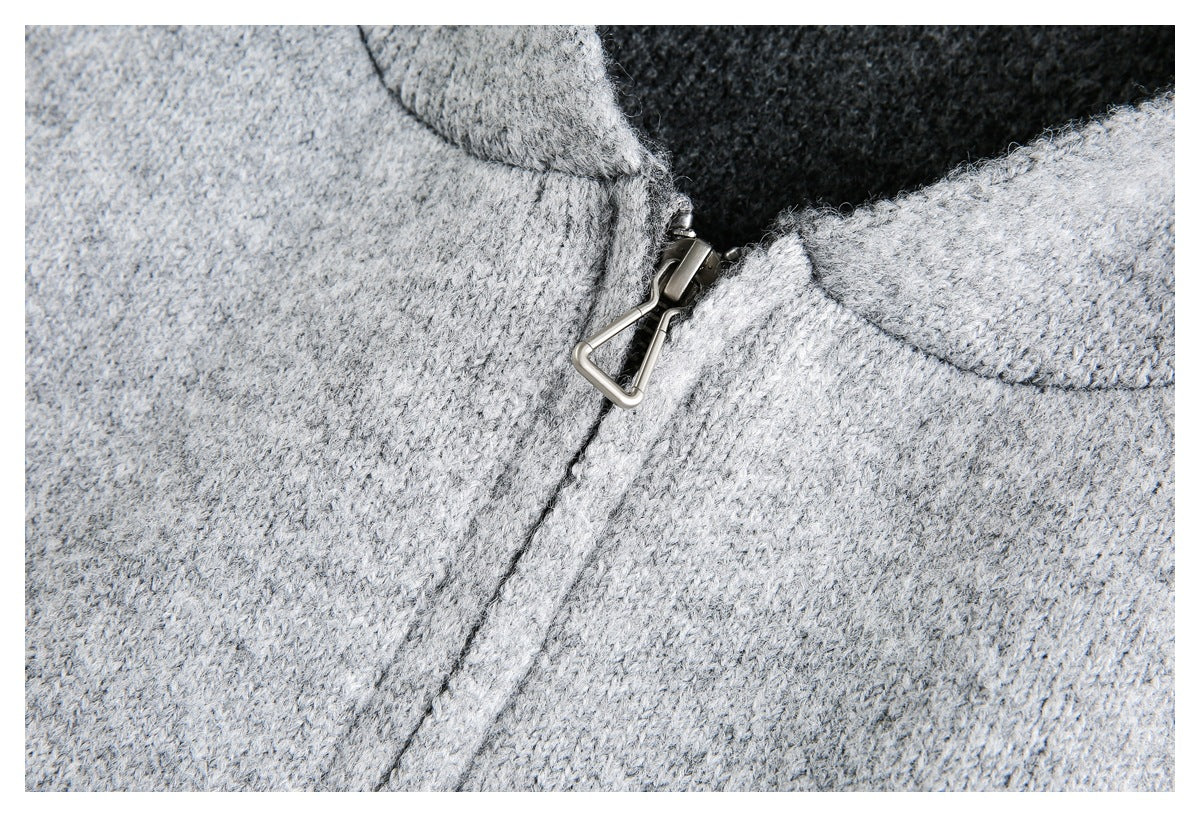 Close-up of a metal zipper pull and front seam on a light gray knit garment.