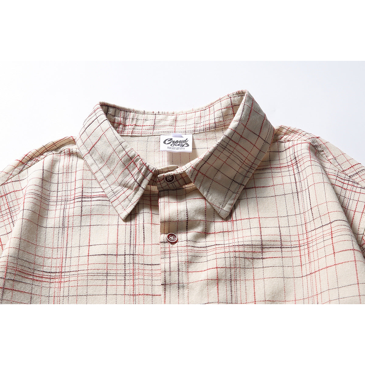 Close-up of an off-white plaid shirt collar and button placket with thin red and gray lines and a visible neck label.