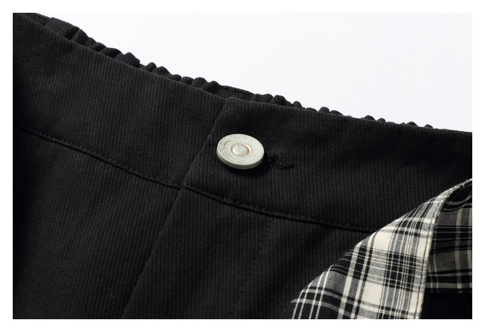 Close-up of a silver button on black trousers beside a black-and-white plaid tie.