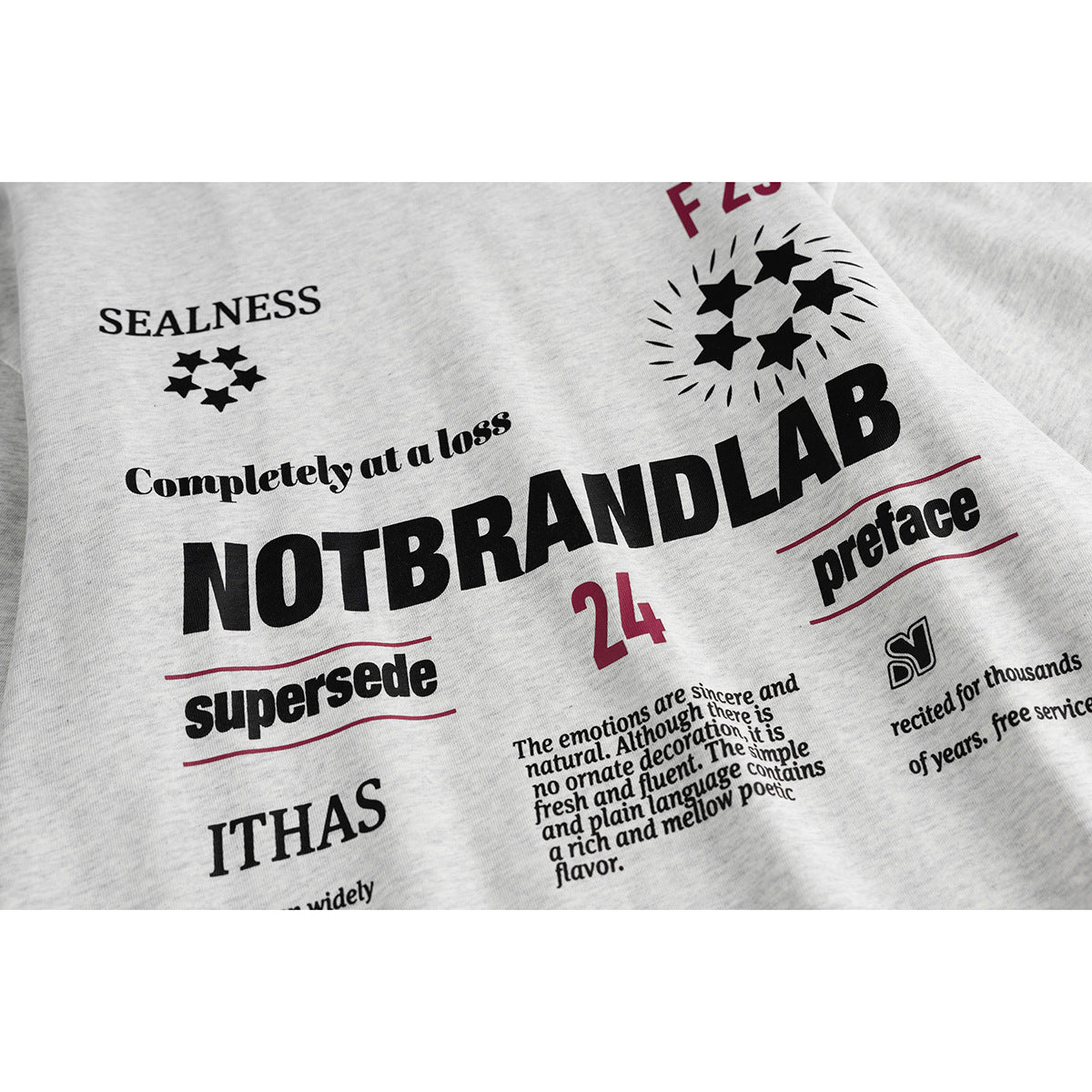 Close-up of the light gray T-shirt's printed black and burgundy text and star graphics.