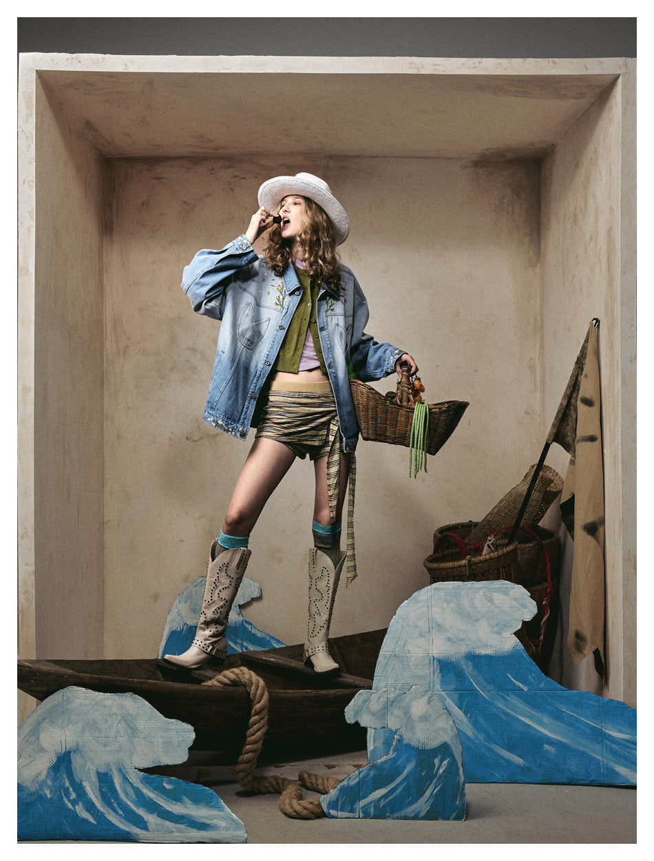 Model wearing an oversized ombre denim jacket open over a green top, with a hat and cowboy boots in a styled set