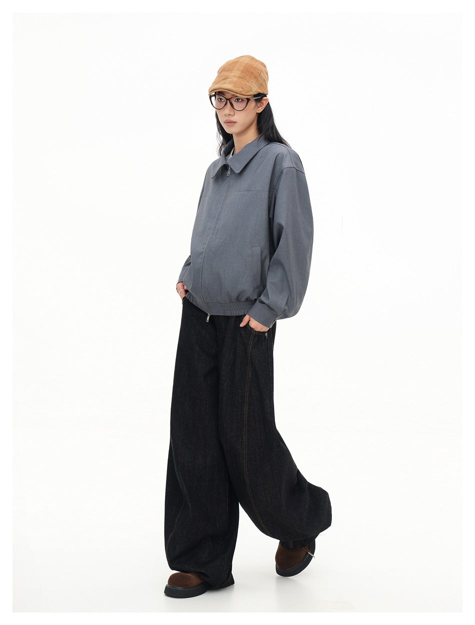 Full-length three-quarter view of a model wearing a gray zip jacket and loose black jeans.