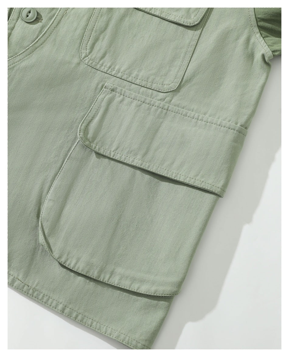 Close-up of a sage-green garment showing layered flap pockets and herringbone fabric.