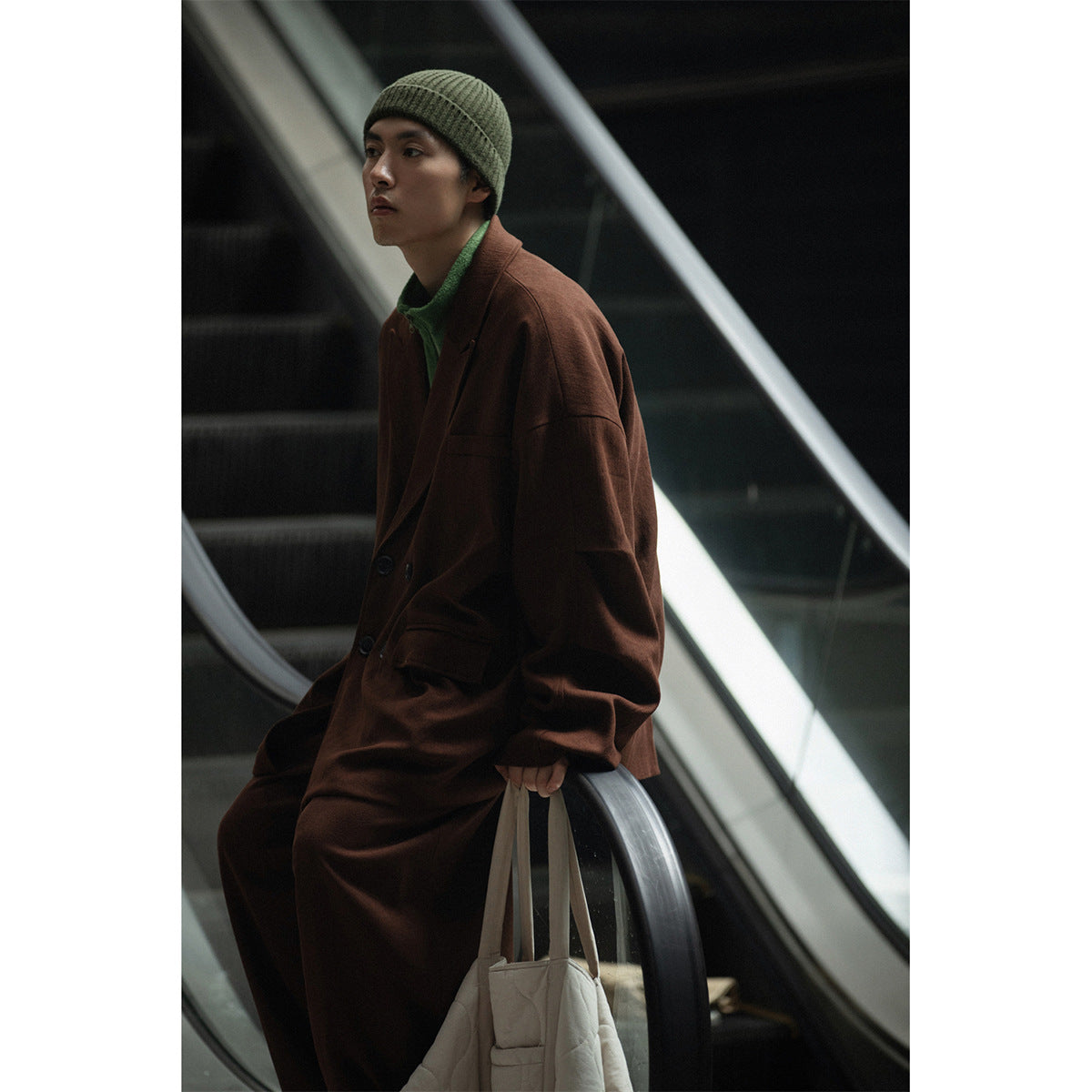 Side view of a model in an oversized brown blazer and trousers, green top, and olive beanie.
