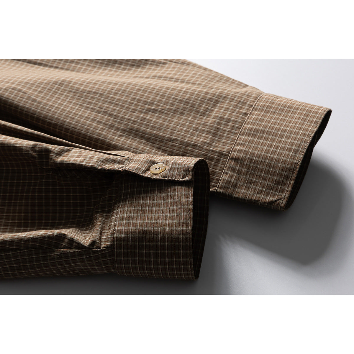 Close-up of the brown plaid shirt's long sleeve and buttoned cuff.