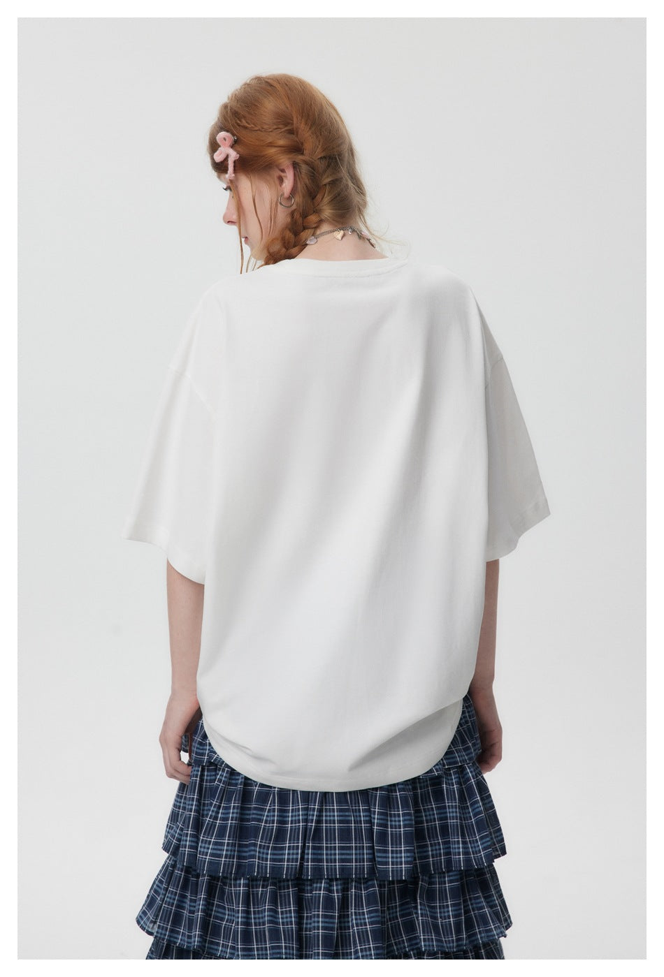 Back view of a model wearing a plain oversized white T-shirt with a navy plaid tiered skirt.