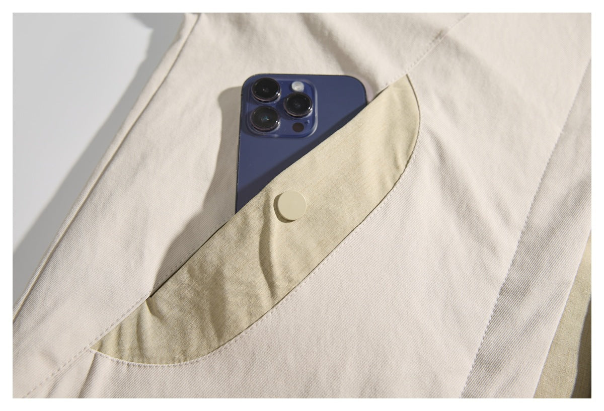 Close-up of a cream jacket pocket with a beige flap and snap fastener holding a smartphone.