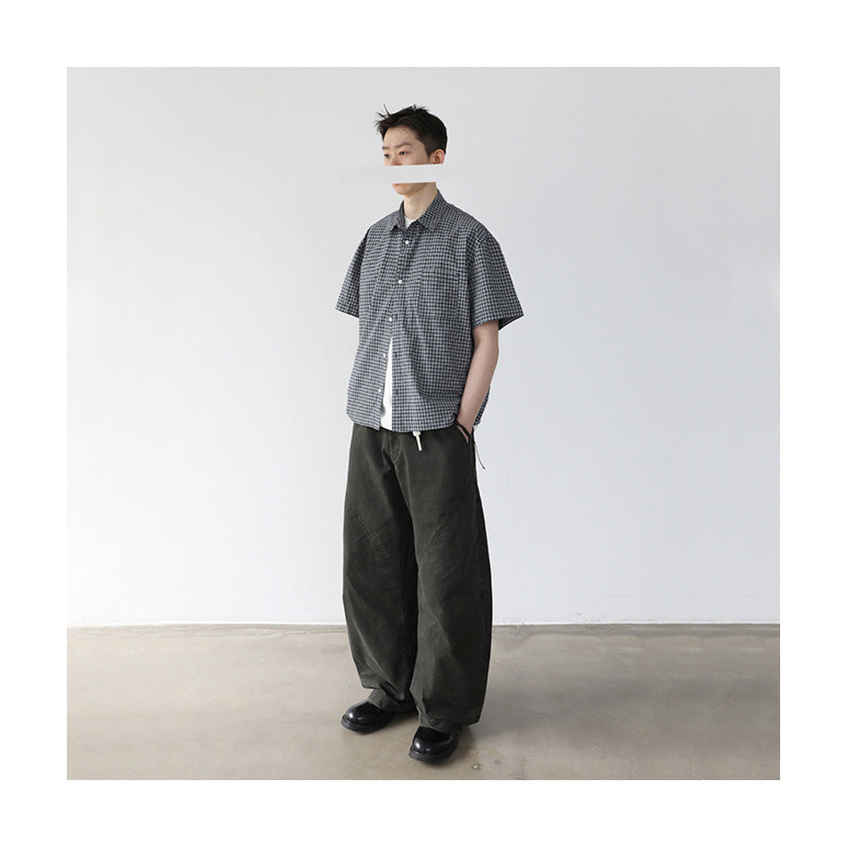Model wearing a short-sleeve black-and-white checked button-up shirt with loose dark trousers.
