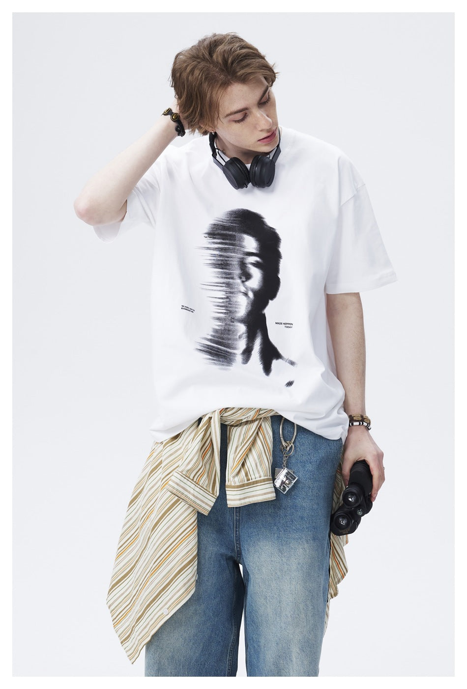 Model wearing an oversized white T-shirt with a large black abstract face graphic and blue jeans.