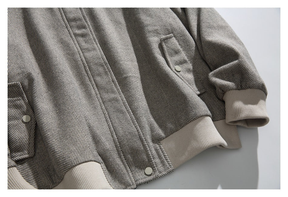 Close-up of a gray herringbone jacket with snap buttons and light beige ribbed cuffs and hem.