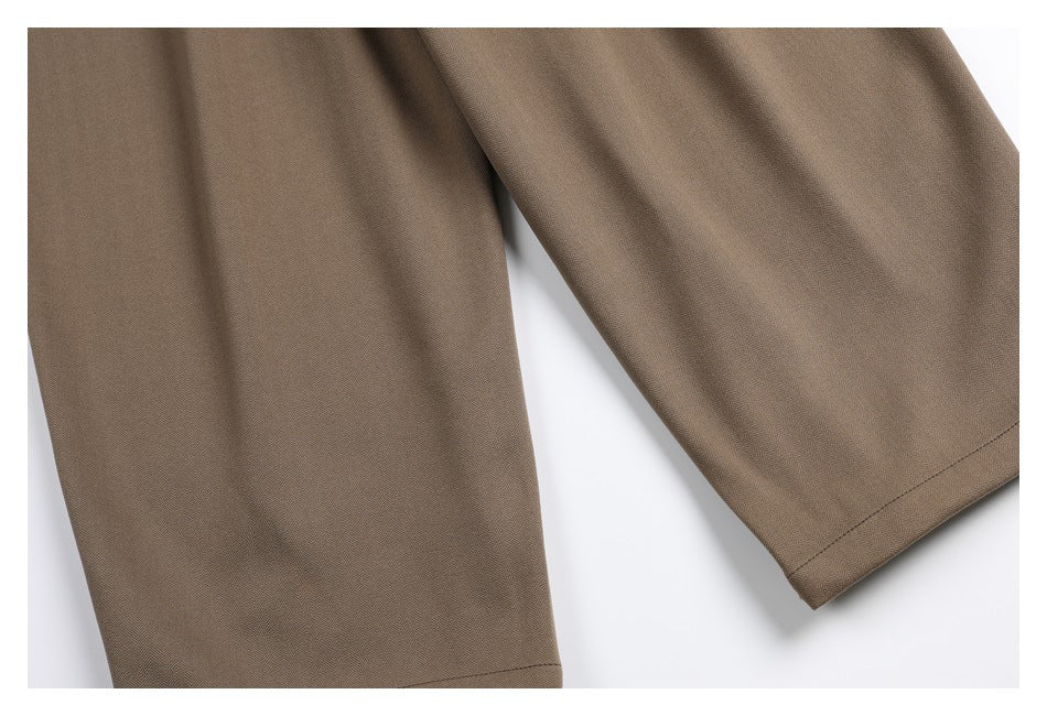 Close-up of the taupe trousers' legs and stitched hems laid flat.