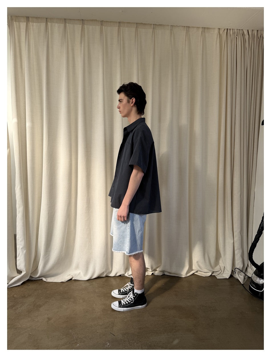 Side view of model wearing the striped short-sleeve shirt with light denim shorts and black sneakers