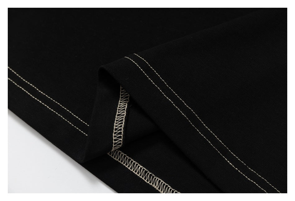Close-up of black garment fabric showing cream double-stitched hem and overlock seam.