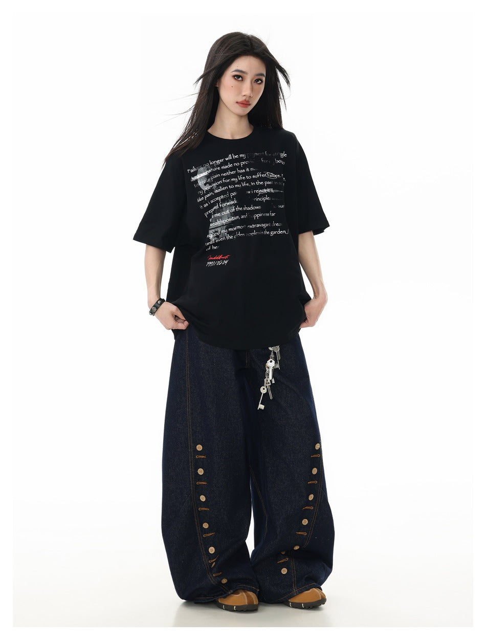 Model wearing the black oversized text-print t-shirt with wide-leg dark denim jeans and brown shoes, full-length view