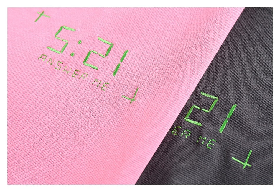 Close-up of pink and charcoal fabric with green embroidered “5:21 ANSWER ME” lettering and crosses.