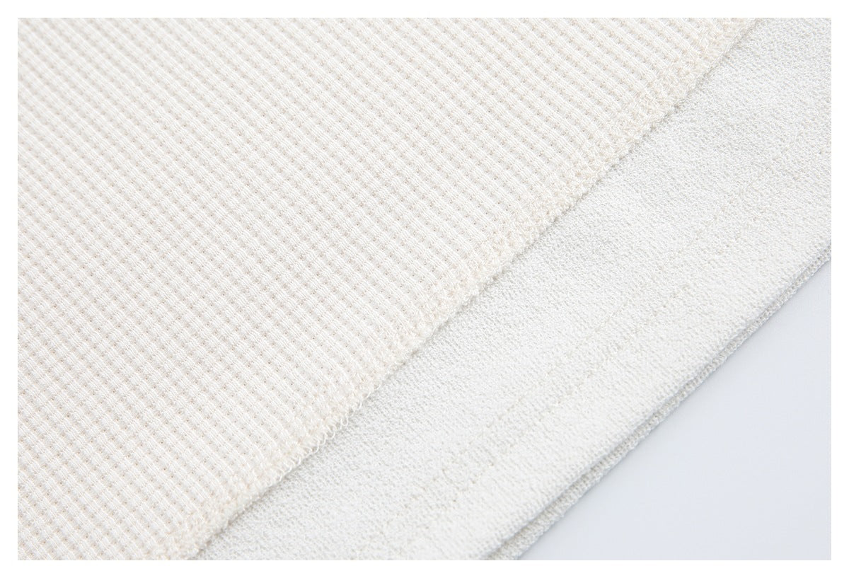 Close-up of an off-white waffle-knit garment hem with visible stitching.