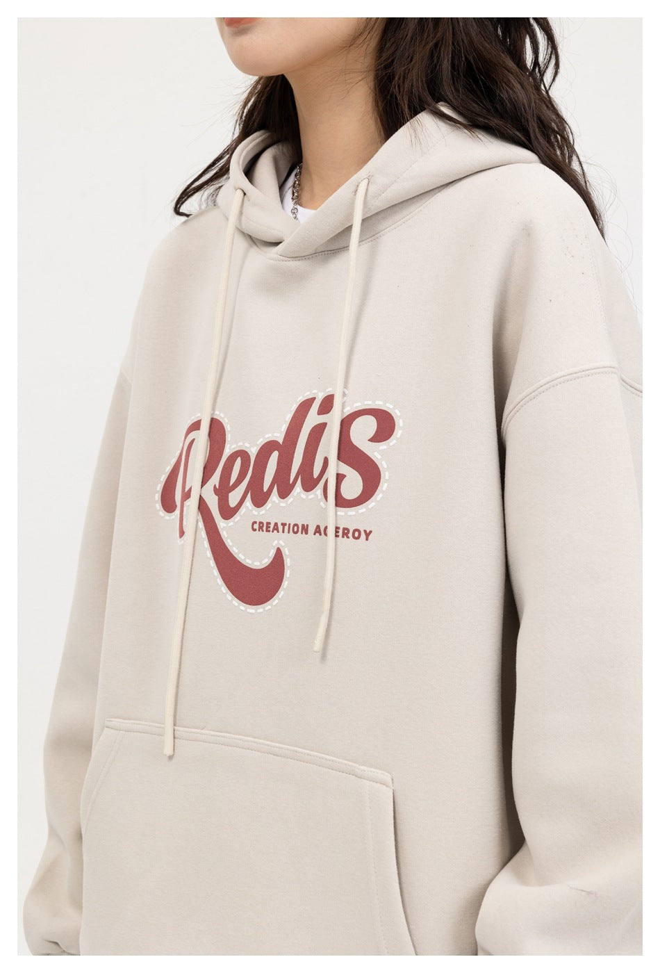 Close-up of a cream hoodie showing its red script chest graphic, drawstrings, hood, and kangaroo pocket.