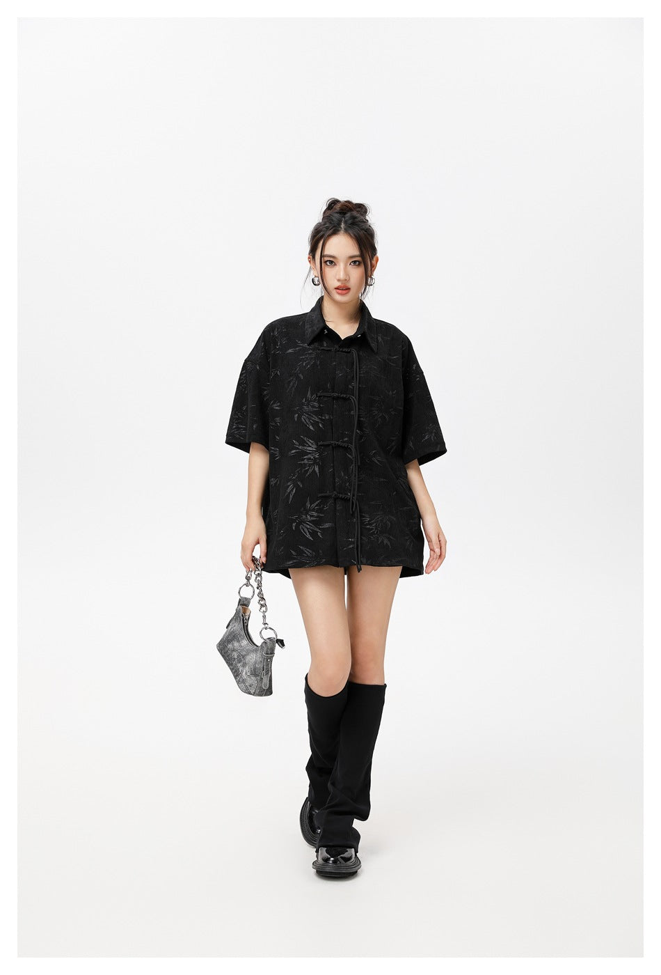 Model wearing an oversized black short-sleeve shirt with a subtle leaf pattern and knotted frog closures.