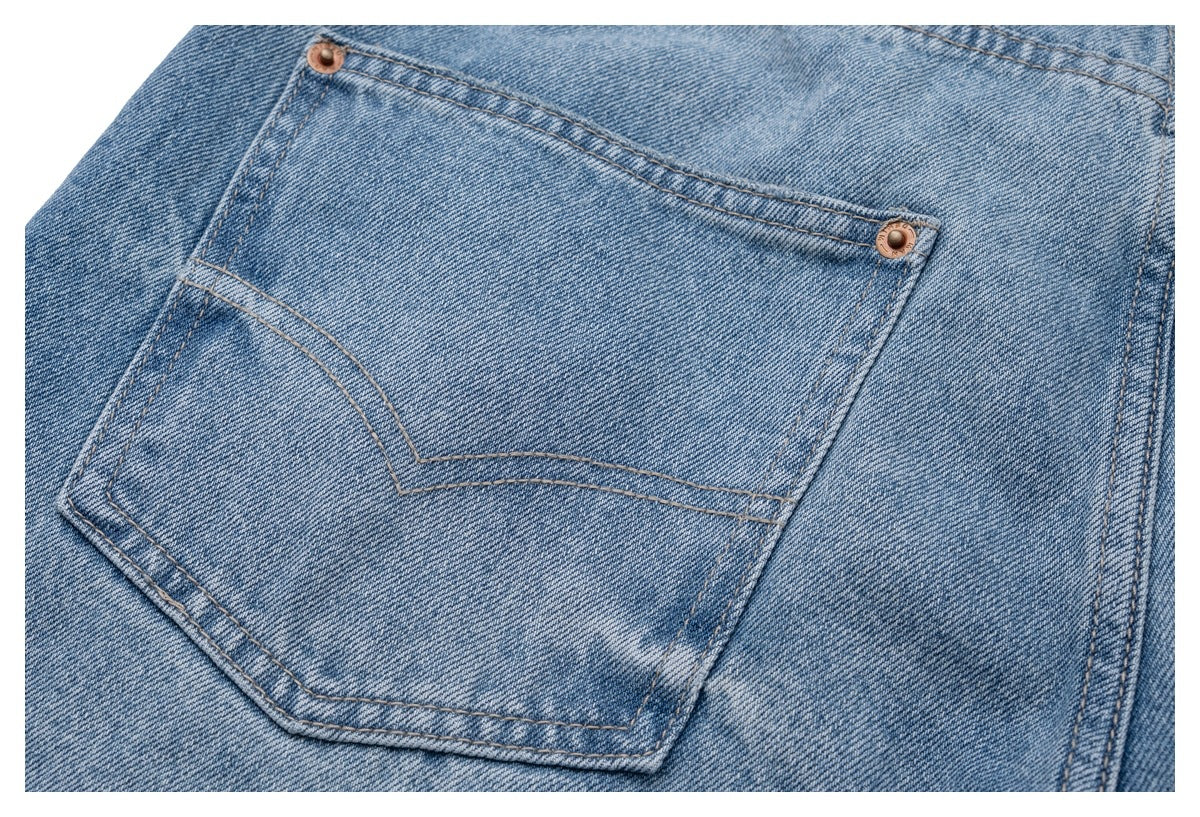 Close-up of a rear pocket on light blue jeans, with curved double stitching and copper-tone rivets.