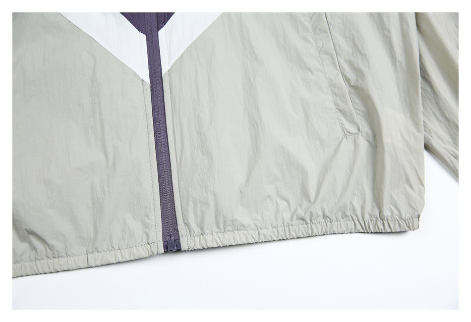 Close-up of the light gray windbreaker’s purple front zipper, white color-block panels, pocket, and gathered hem.
