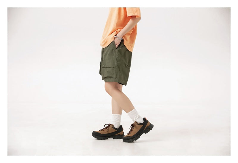 Side view of a model wearing olive green cargo shorts with an orange T-shirt and hiking shoes.