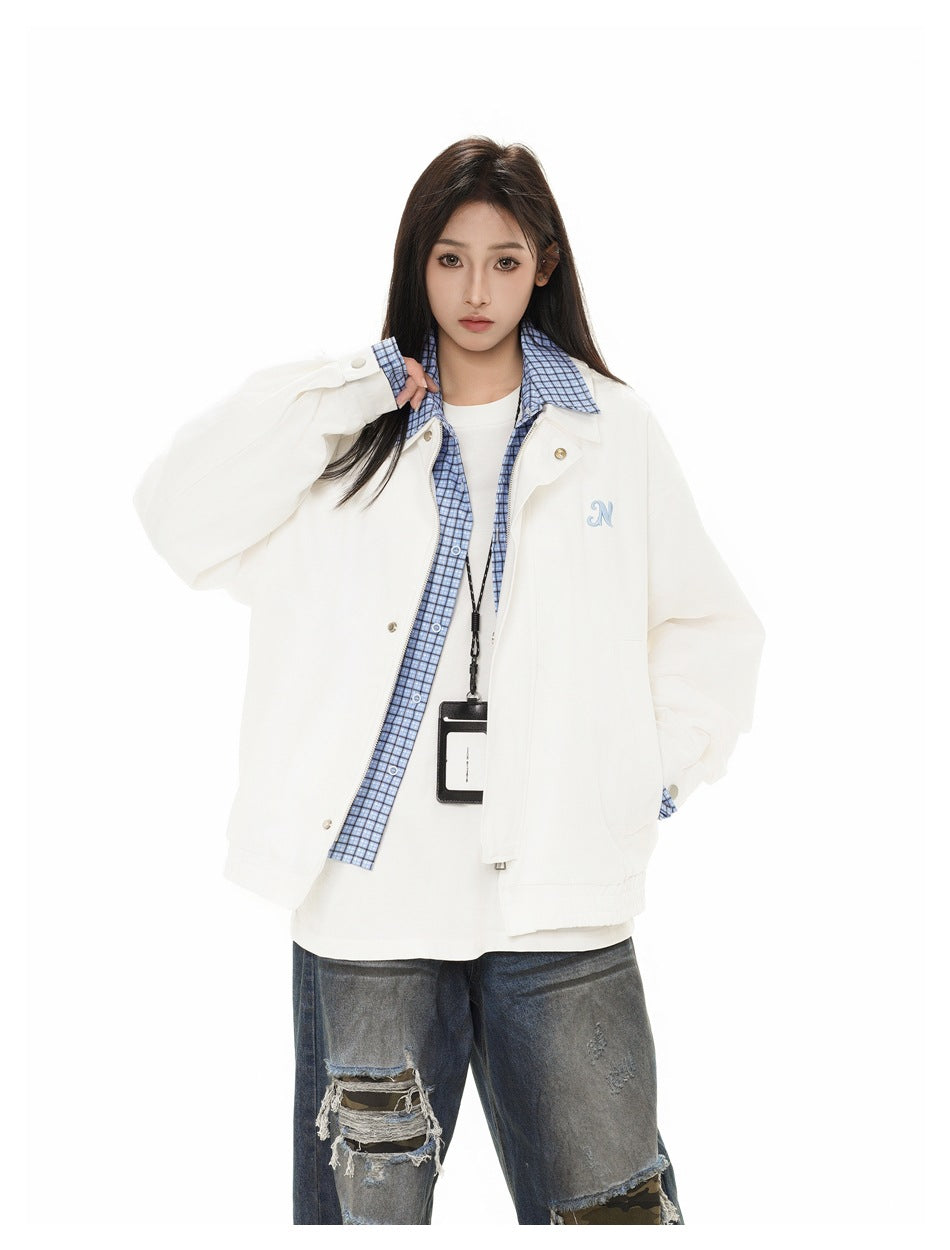Model in a white oversized jacket with blue checked trim over a white top, paired with distressed jeans.