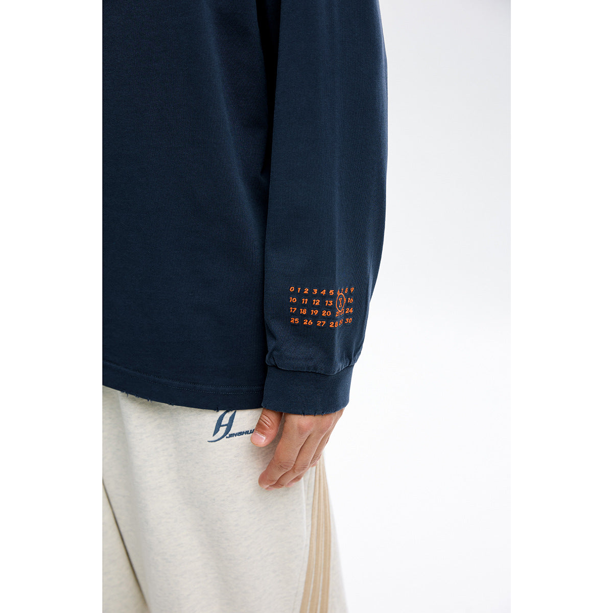 Close-up of the navy shirt cuff with small orange number graphics, above cream pants.