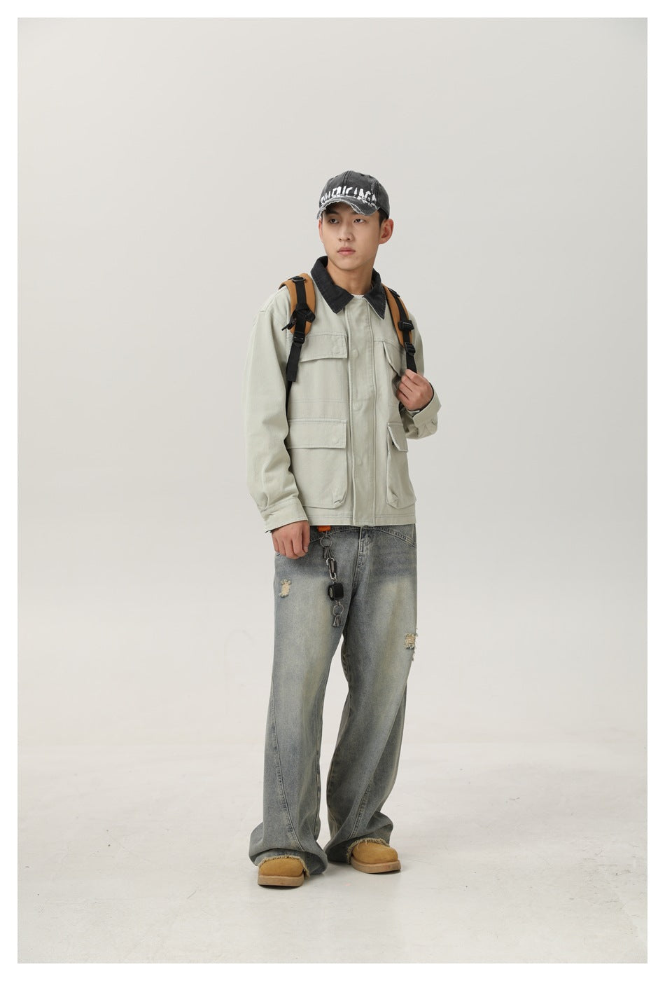 Full-length model wearing a pale gray-green utility jacket with a dark collar, jeans and a backpack.