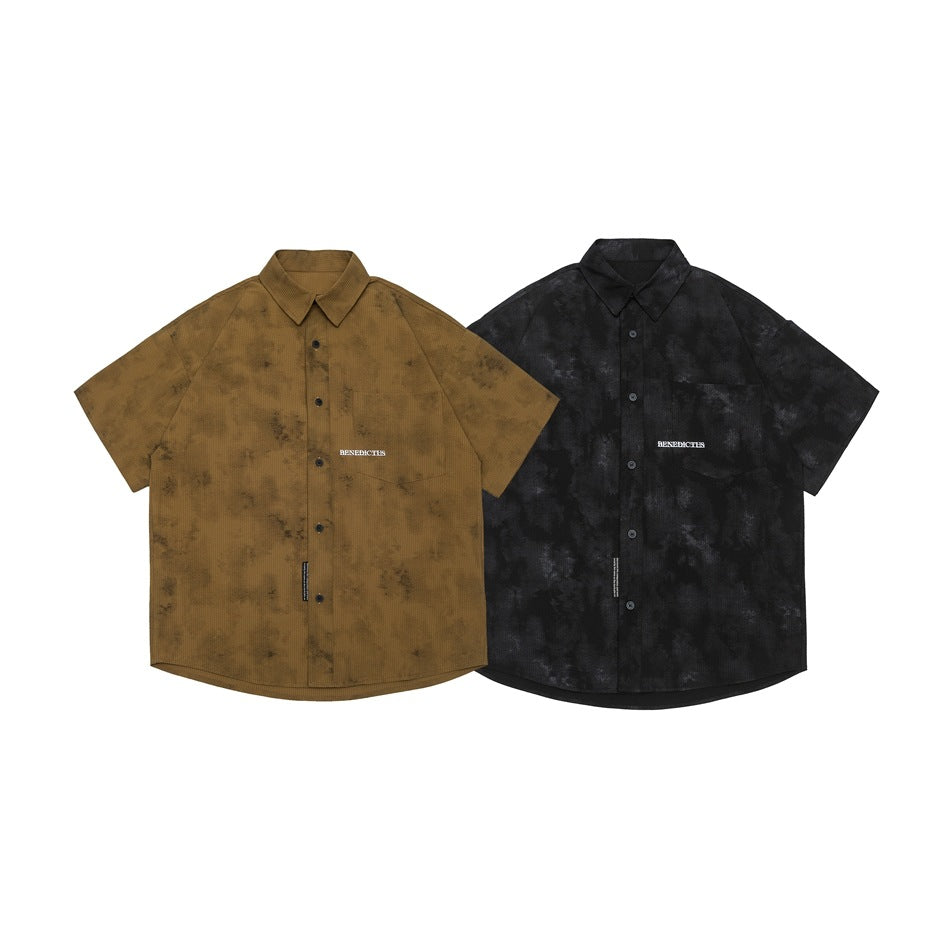 Front view of short-sleeve button-up shirts in brown and black, both with mottled patterns and small chest lettering.