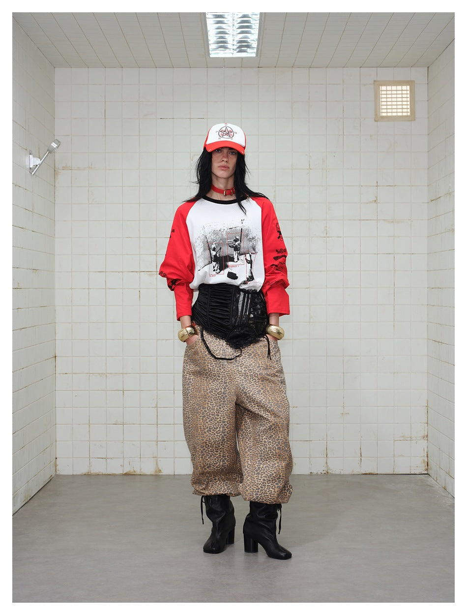 Front-facing model wearing a white graphic raglan shirt with red sleeves, a black corset and leopard-print trousers.