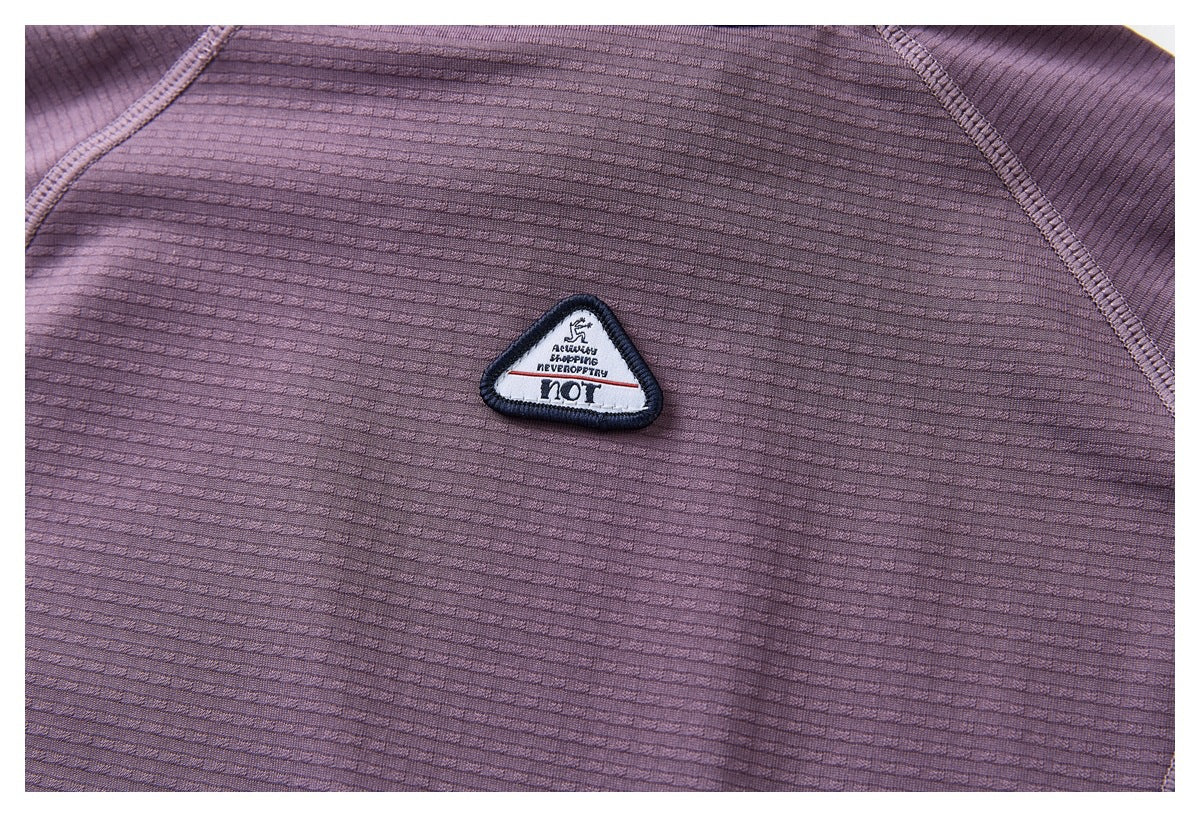 Close-up of a purple ribbed garment with a small triangular embroidered patch bearing English lettering.