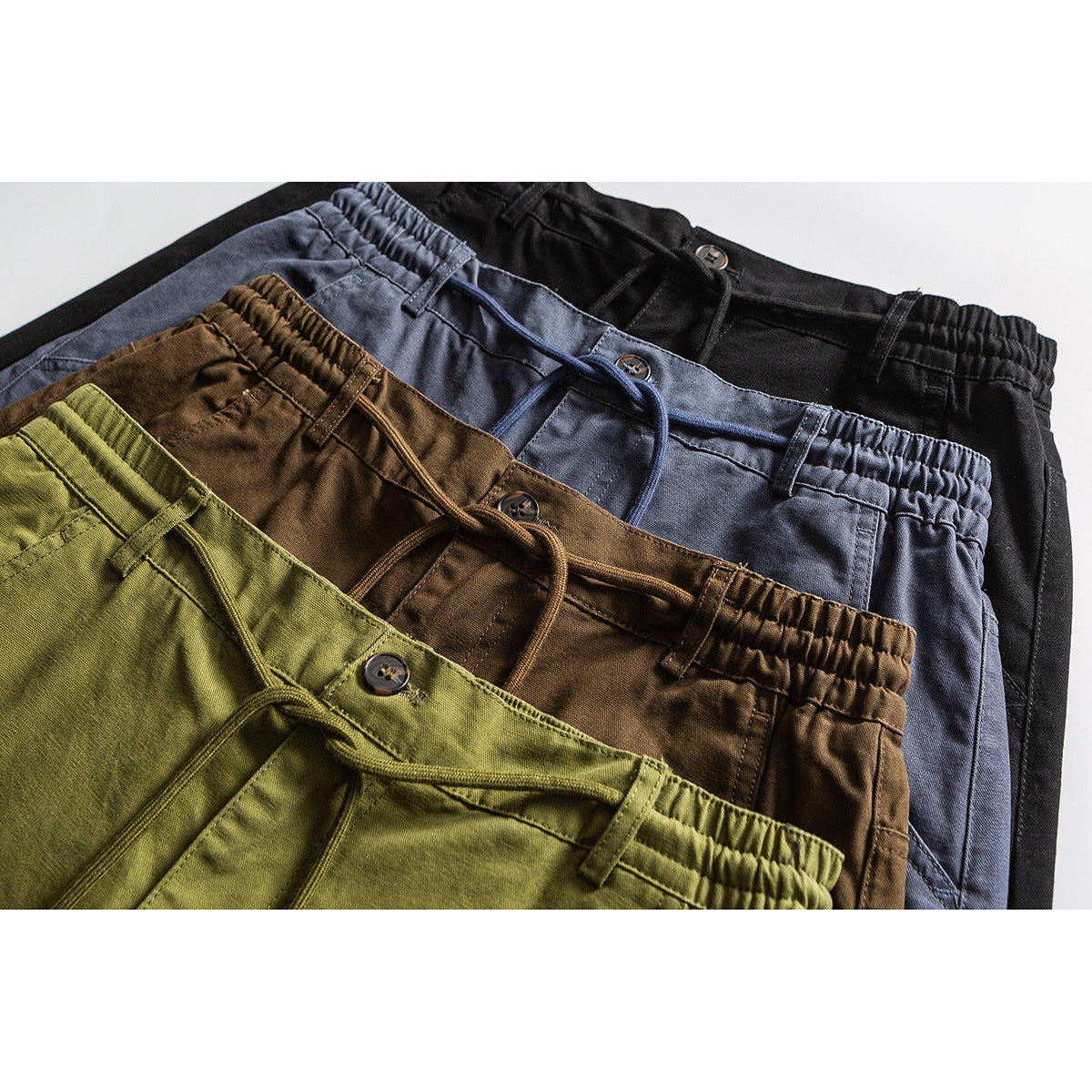 Close-up of four pairs of drawstring pants in olive, brown, slate blue, and black, showing elastic waistbands and buttons.