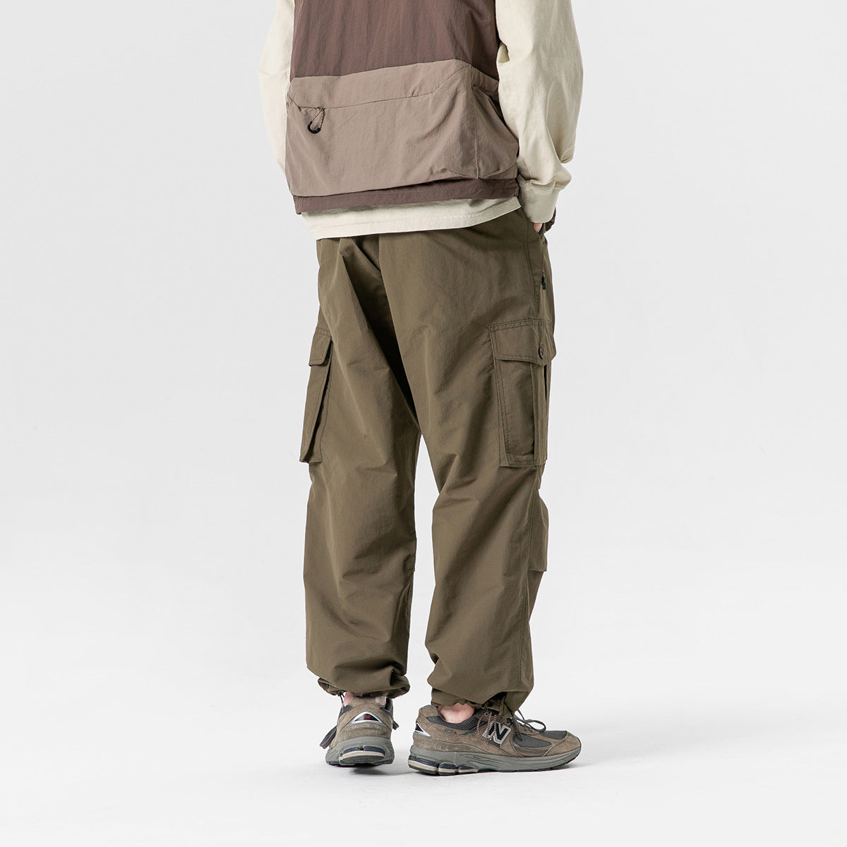 Rear view of a model wearing olive cargo pants with large flap pockets and elasticated ankle cuffs.