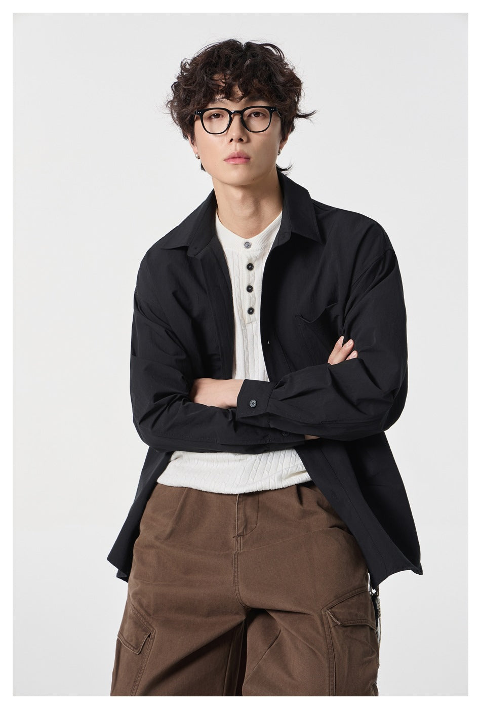 Model wearing a loose black button-up shirt over a white knit top and brown cargo trousers.