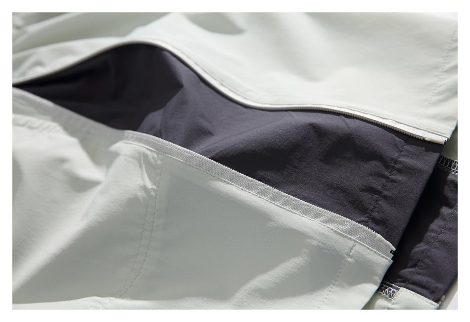 Close-up of pale gray pants opened to show a dark inner panel and layered pocket construction.