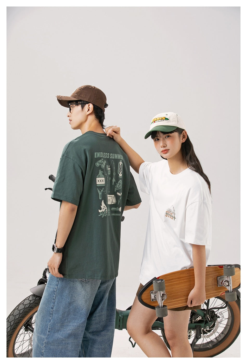 Model shows the large back graphic of a dark green tee beside another model in a white graphic tee.