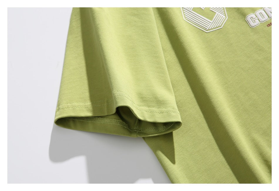 Close-up of a short sleeve and part of the white chest embroidery on a light olive-green T-shirt.