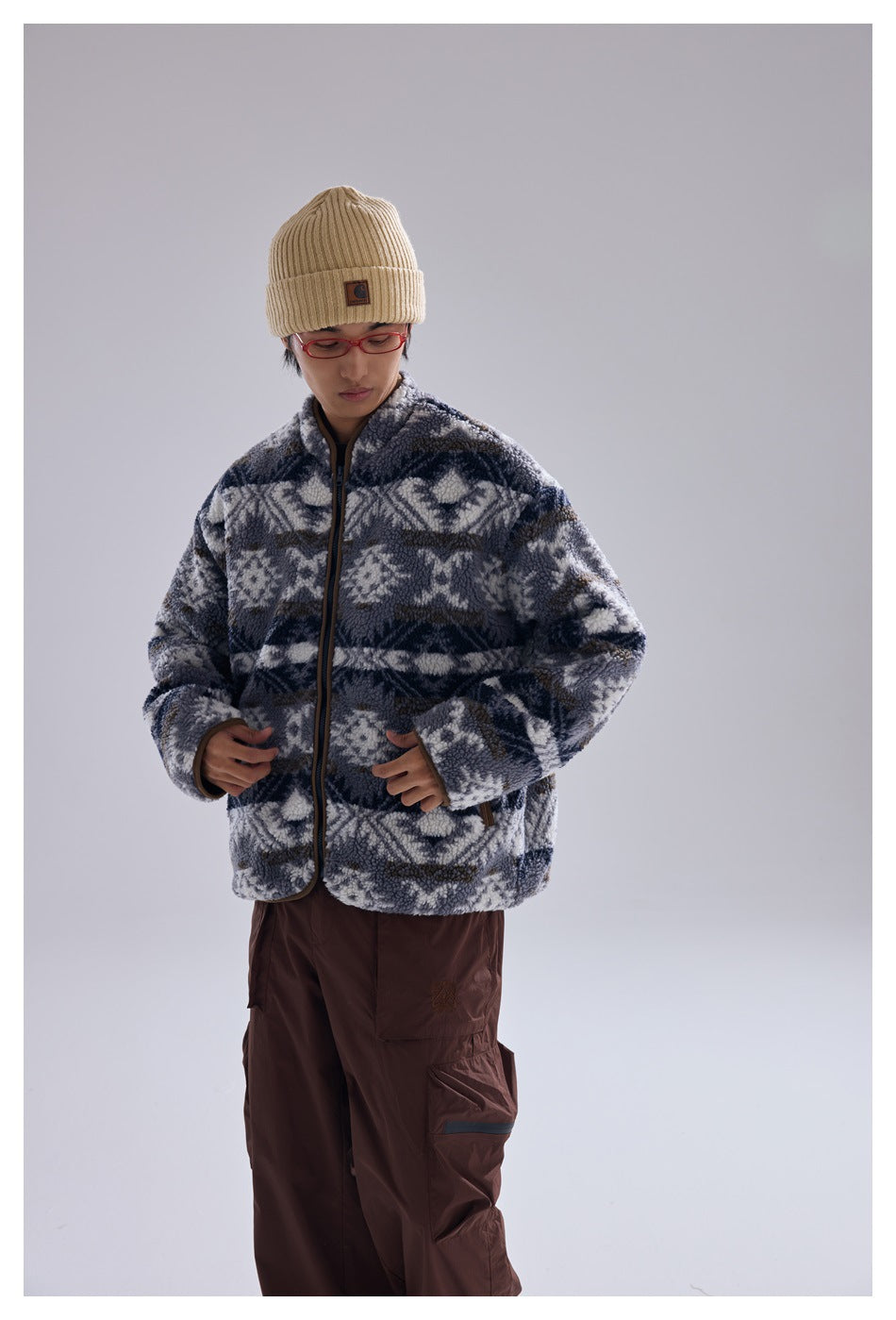 Front view of a model wearing a zipped blue-gray and white geometric fleece jacket with brown-trimmed pockets.