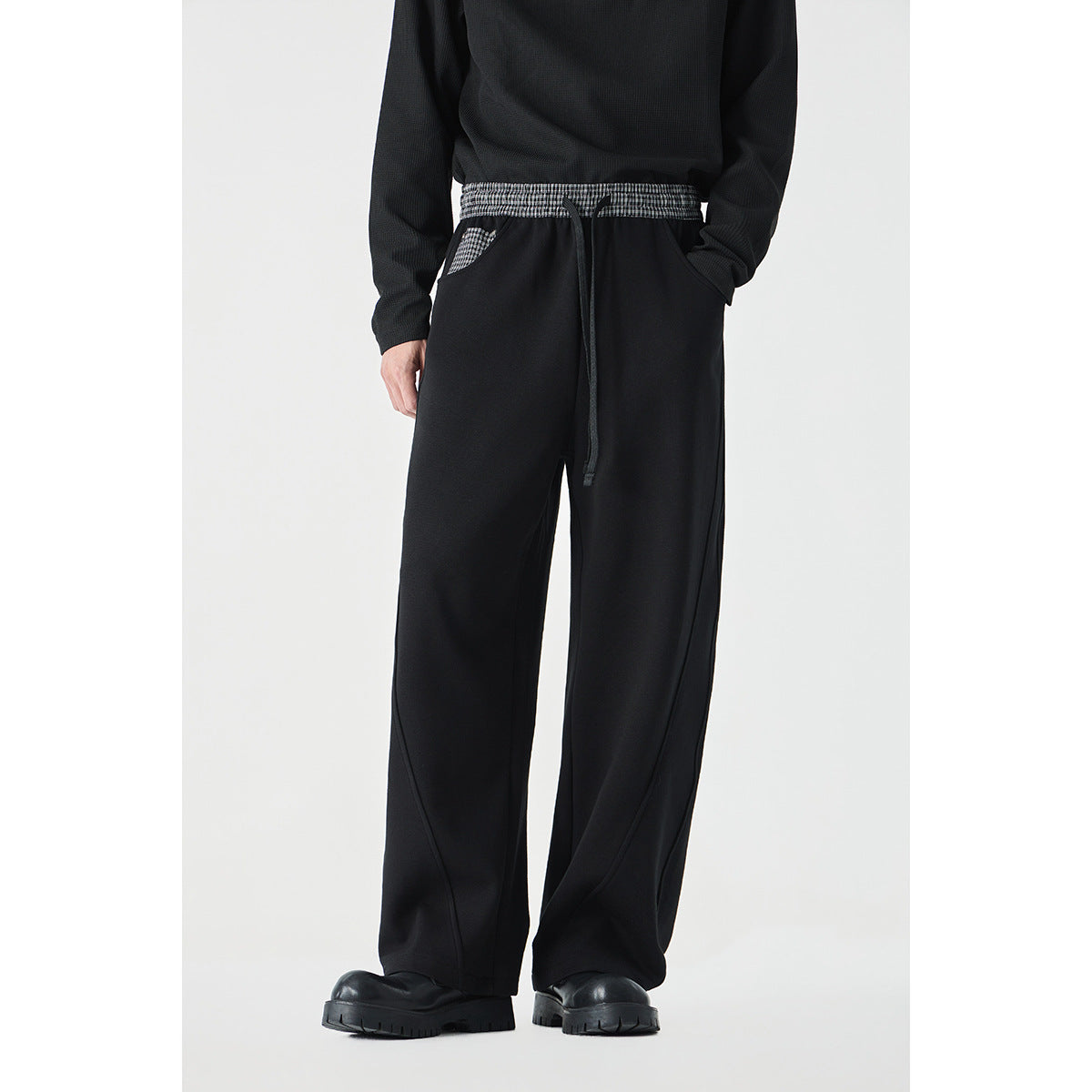 Front view of a model wearing black wide-leg pants with a checked elastic waistband, drawstring, and checked pocket trim.