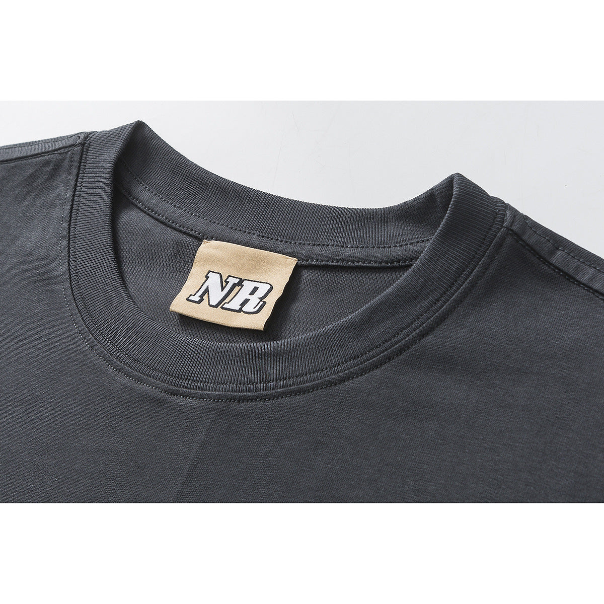 Close-up of a dark charcoal T-shirt's ribbed crew neck and beige inner label marked “NB.”