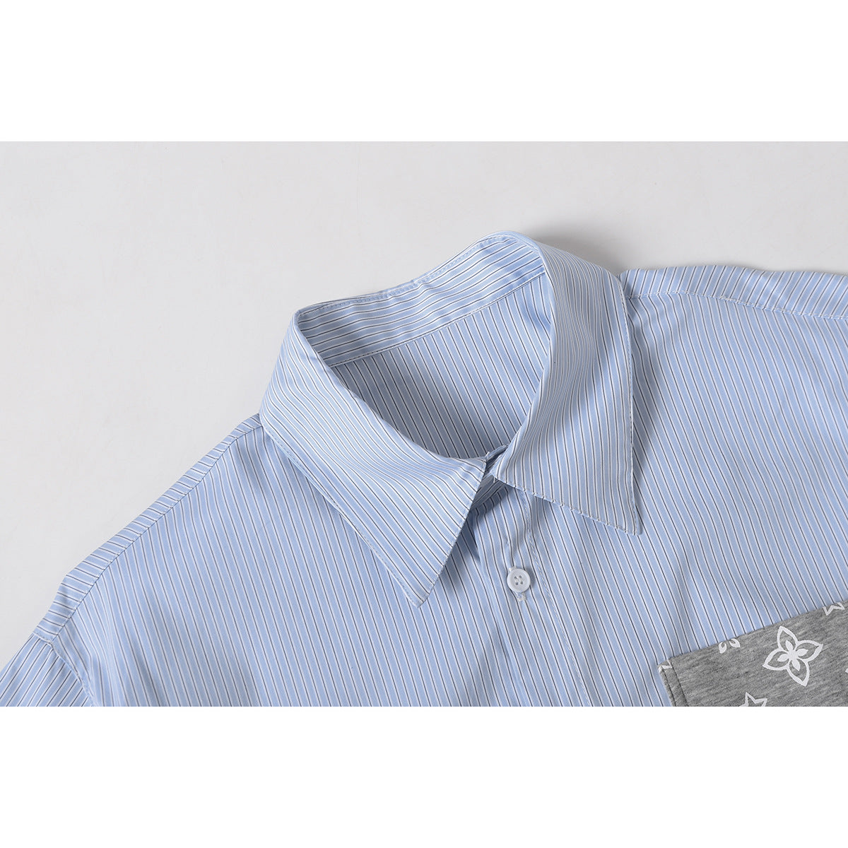 Close-up of a light blue striped shirt collar, button, and edge of a gray printed pocket.