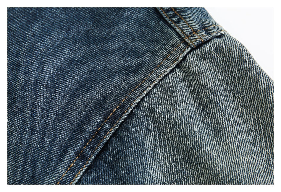 Close-up of dark blue denim fabric and a diagonal seam with tan stitching.