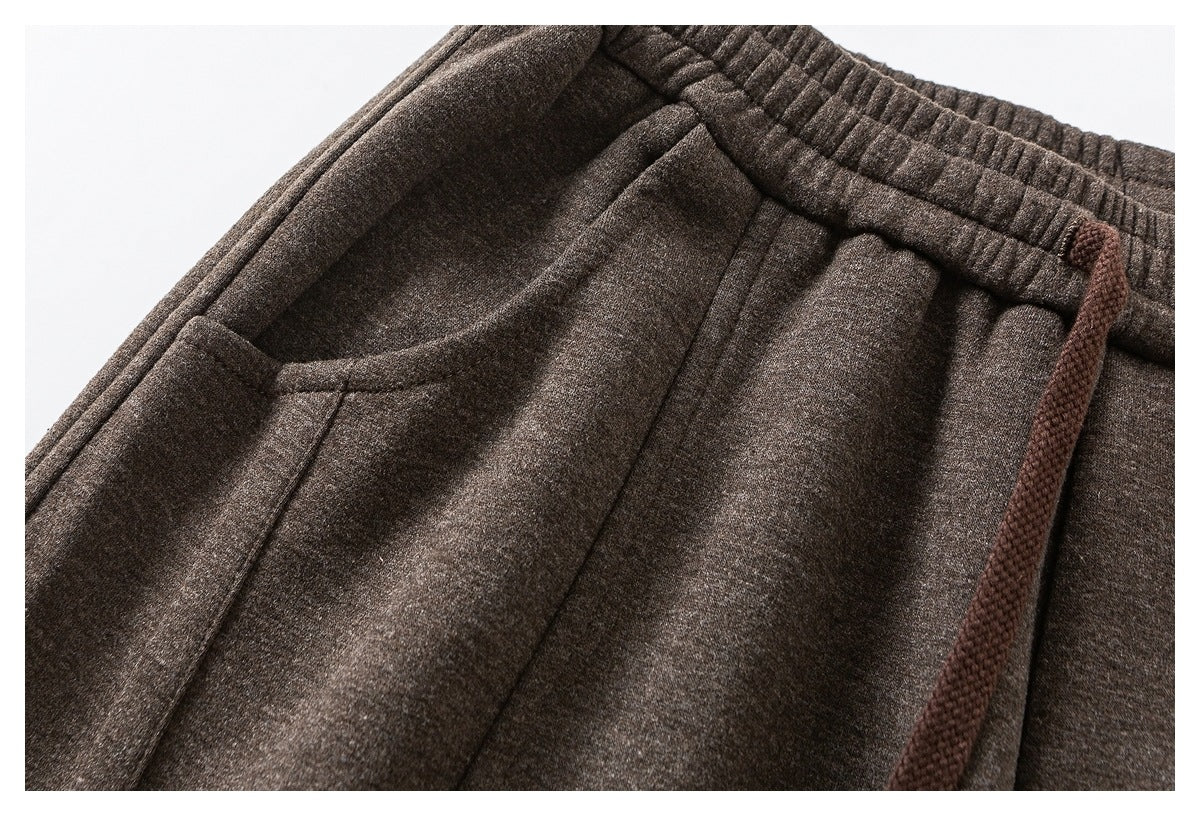 Close-up of brown trousers showing the elastic waistband, drawstring and curved front pocket.