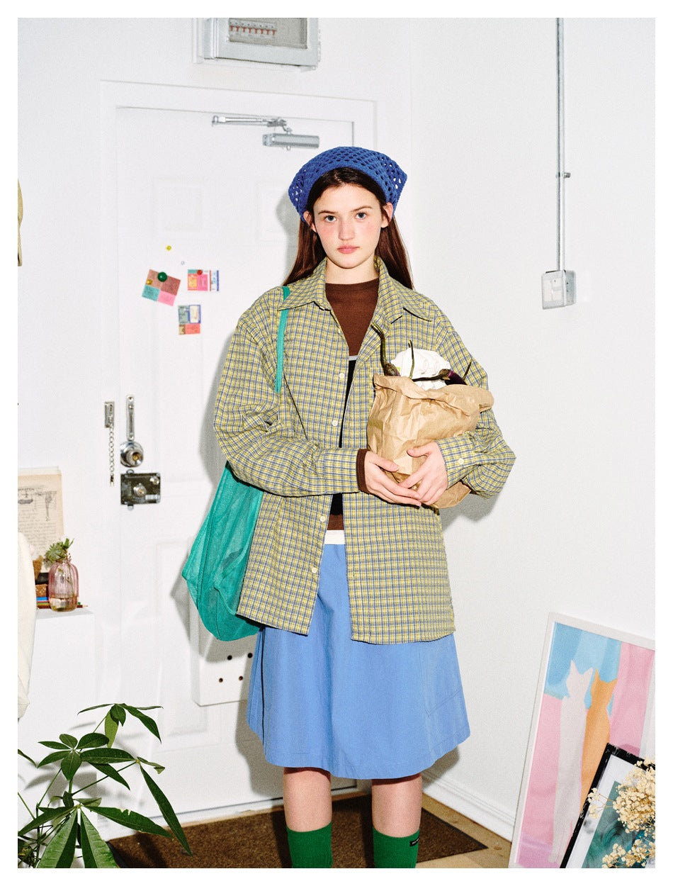 Model wearing a yellow and blue plaid button-up shirt over a brown top and blue skirt, with a blue knit hat.