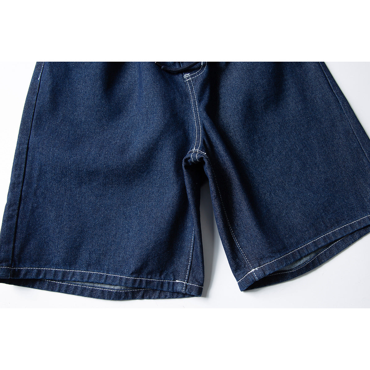 Close-up of dark indigo denim shorts showing the crotch seam and wide leg hems with white topstitching.