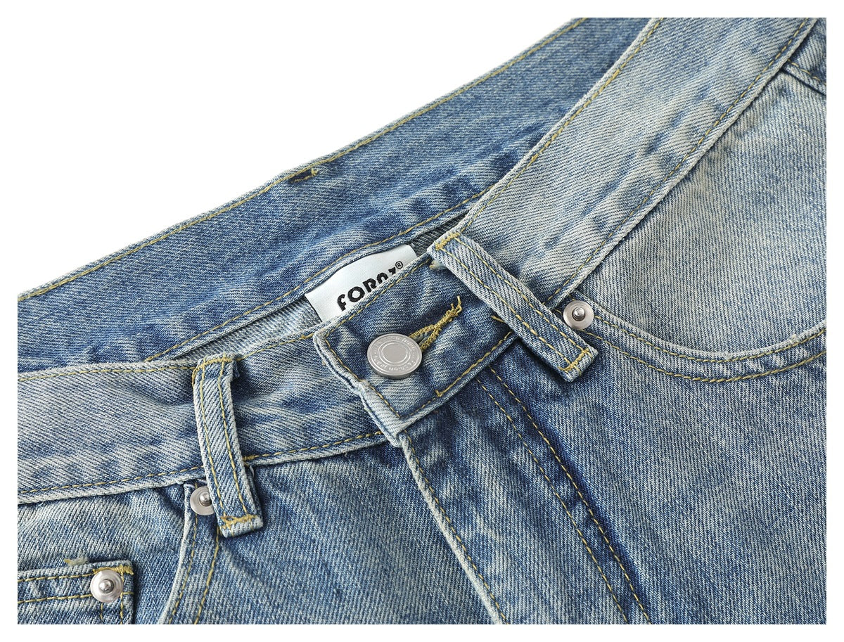 Close-up of the jeans’ front waistband, button, belt loops and faded blue denim.