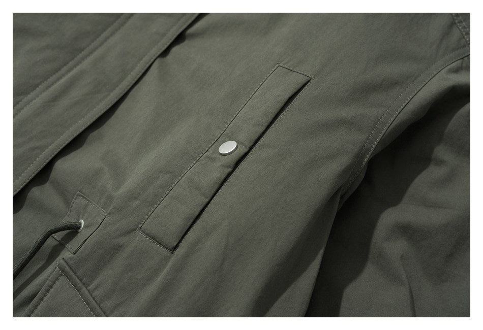 Close-up of an olive jacket pocket with a narrow flap and silver snap button.