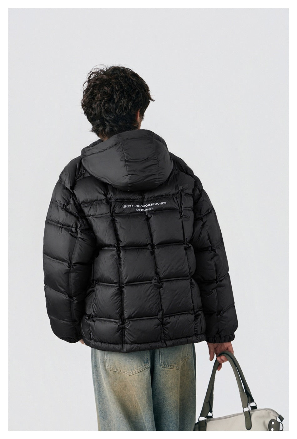 Back view of a model wearing a black hooded puffer jacket with quilted panels and jeans.
