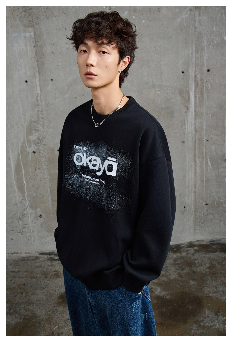 Angled view of a model wearing a black oversized sweatshirt with a distressed white chest graphic.