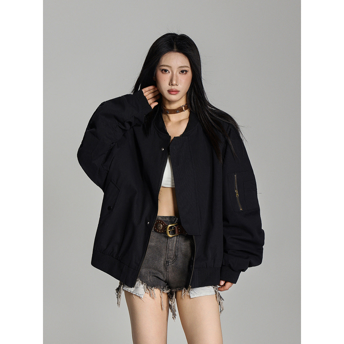 Model wearing an oversized black bomber jacket with a zip sleeve pocket, shown from the front.
